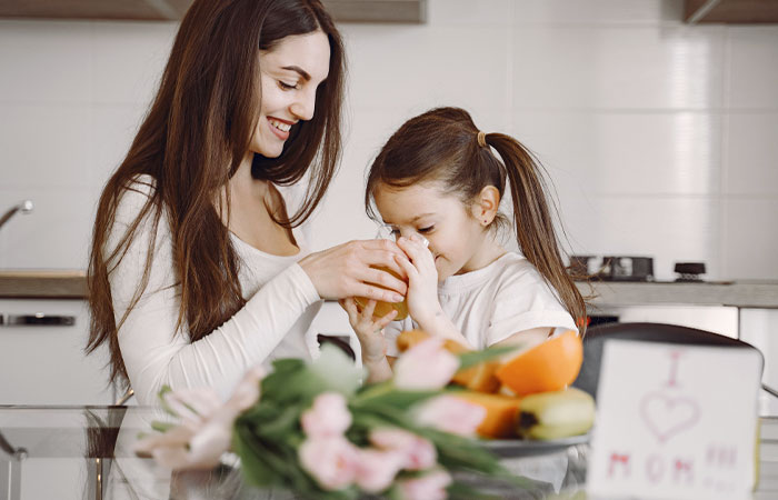 Madre en la cocina con su hija dándole de beber